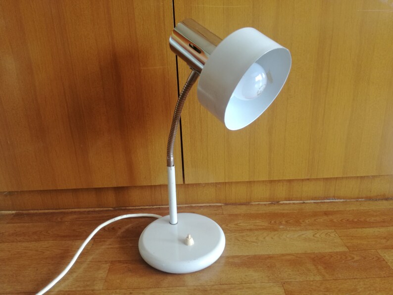 May include: A white desk lamp with a flexible arm and a white shade. The lamp has a chrome base and a chrome switch.