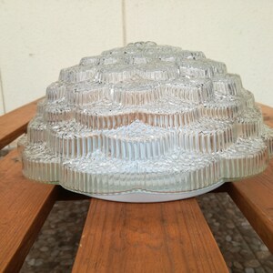 May include: A clear glass ceiling light fixture with a textured, flower-like design. The light fixture is made of multiple layers of glass, creating a unique and intricate pattern.