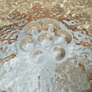 May include: Close-up of a clear glass surface with a textured pattern of raised circles. The circles are arranged in a flower-like shape in the center of the image.