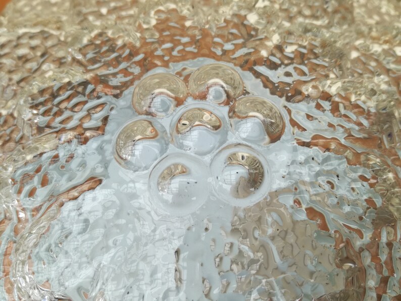 May include: Close-up of a clear glass surface with a textured pattern of raised circles. The circles are arranged in a flower-like shape in the center of the image.