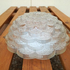 May include: A clear glass ceiling light fixture with a textured, geometric design. The light fixture is shaped like a dome and has a scalloped edge.