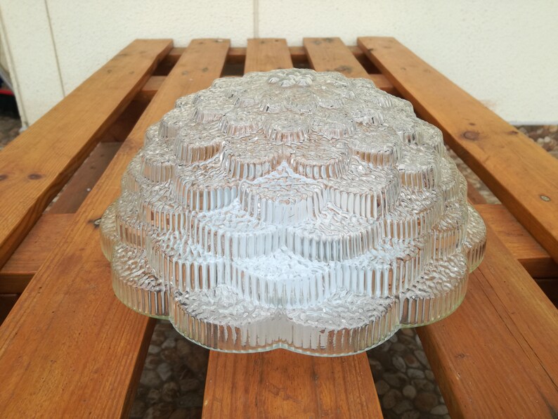 May include: A clear glass ceiling light fixture with a textured, geometric design. The light fixture is shaped like a dome and has a scalloped edge.