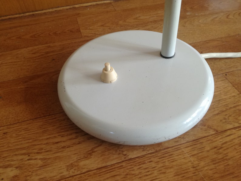 May include: A white lamp base with a round, flat top and a white cord. The base has a small, off-white switch on the top.