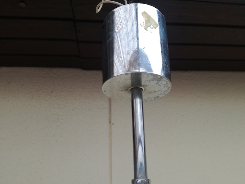 Puede incluir: Primer plano de una l&aacute;mpara de techo plateada con una base redonda cromada y una varilla larga, delgada y plateada.