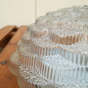 May include: A clear glass lampshade with a textured, geometric design. The shade is made up of multiple layers of glass, each with a different pattern.