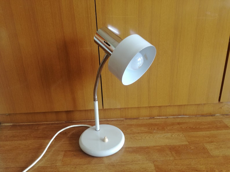 May include: A white desk lamp with a flexible arm and a white shade. The lamp has a silver base and a white cord.