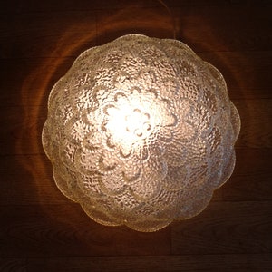 May include: A clear glass ceiling light fixture with a textured, floral design. The light is on and illuminating the room.