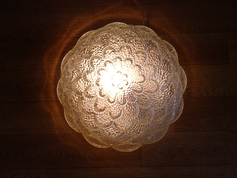 May include: A clear glass ceiling light fixture with a textured, floral design. The light is on and illuminating the room.