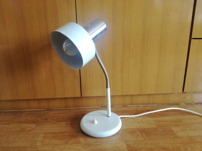 May include: A white and chrome desk lamp with a flexible arm and a white shade. The lamp is on a wooden floor.