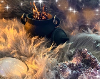 May include: A black cauldron with a lid sits on a fluffy white and brown fur surface. The cauldron is filled with glowing embers and sparks. The background is blurred and features a soft, light blue colour with sparkling lights.