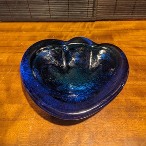 May include: A blue glass ashtray shaped like a heart with a green interior.