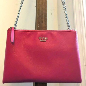 May include: A bright pink chain strap purse with a gold Guess logo. The purse has a zipper closure.