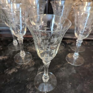 May include: A collection of clear, stemmed wine glasses. Each glass features an etched floral design on the bowl. The glasses have a classic shape with a round base and a slender stem.