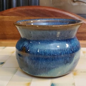 May include: A small, blue and brown ceramic pot with a rounded body and a slightly flared rim. The pot has a mottled glaze with shades of blue and green.