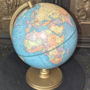 May include: A vintage globe with a blue ocean and colorful continents. The globe is mounted on a gold-colored metal base and has a gold meridian ring. A classic educational or decorative item.