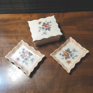 May include: Three white ceramic trinket dishes with pink and gold scalloped edges. Each dish features a floral design with pink, blue, and yellow flowers.