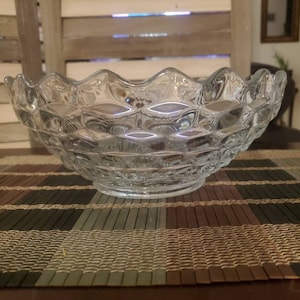 May include: A clear glass bowl with a scalloped rim and a textured, diamond-shaped pattern. The bowl is sitting on a woven placemat.
