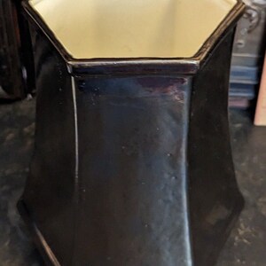 May include: A black octagonal ceramic vase with a white interior. The vase has a smooth, glossy finish.