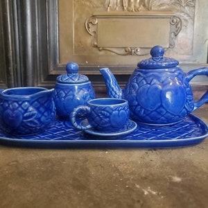 May include: A blue ceramic tea set with a teapot, creamer, sugar bowl, cup and saucer, and a tray. The set features a raised heart design.