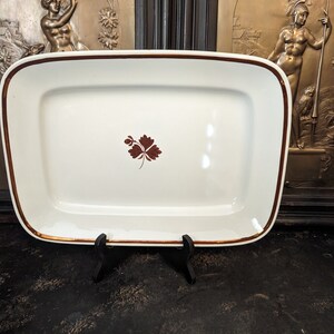May include: A white rectangular serving platter with a gold rim and a brown leaf design in the center.