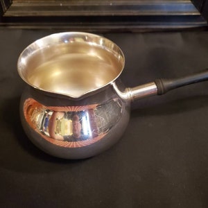 May include: A silver gravy boat with a black handle. The boat is round and has a smooth, polished surface.