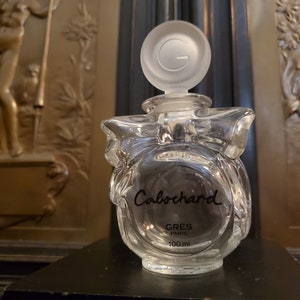 May include: A clear glass bottle of perfume with a bow-shaped design. The bottle is labeled "Calocard GRES PARIS 100 ml".