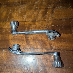 May include: Two chrome window crank handles with a knurled knob on each end. The handles are in good condition and have a shiny finish.