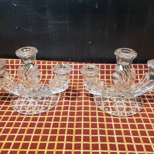 May include: A pair of clear glass candle holders with three candle cups each. The holders have a swirling design and a round base.