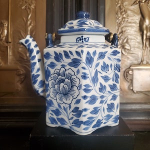 May include: A blue and white porcelain teapot with a floral design. The teapot has a hexagonal shape and gold accents on the handles.