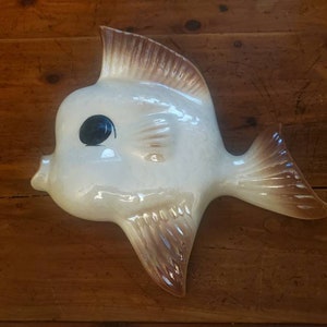 May include: A white ceramic fish wall decor with brown accents. The fish has a large, round body and a single black eye.