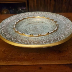 May include: A vintage ceramic ashtray with a white and gold design. The ashtray has a raised rim and a scalloped edge. The center of the ashtray is a smaller, round bowl.