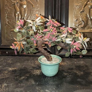 May include: A jade bonsai tree with pink and white flowers in a green ceramic pot. The tree is made of jade and the flowers are made of glass.