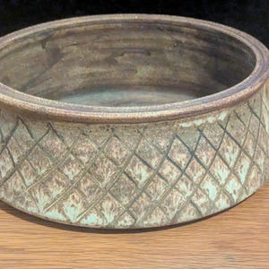 May include: A handcrafted ceramic bowl with a diamond pattern on the exterior. The bowl has a wide, shallow design with a light brown and tan color scheme. The rim is a darker brown, and the bowl sits on a wooden surface.
