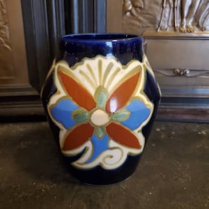 May include: A blue ceramic vase with a colorful floral design. The vase has a rounded body and a wide mouth.