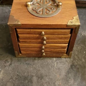 May include: A set of six wooden coasters with a brass trim and a decorative metal handle. The coasters are stacked on top of each other and have a natural wood finish.