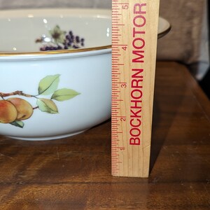K&ouml;nnte beinhalten: Eine wei&szlig;e Porzellanschale mit goldfarbenem Rand und einem Blumendesign mit &Auml;pfeln und Bl&auml;ttern. Die Schale hat einen Durchmesser von 10 cm und steht auf einer Holzoberfl&auml;che neben einem Lineal.