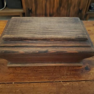 May include: A dark brown wooden box with a hinged lid. The box has a simple, rectangular shape and a smooth, polished finish.