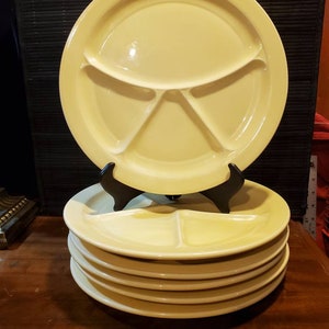 May include: A stack of five yellow divided plates. The plates are made of ceramic and have a smooth, glossy finish. The top plate is slightly larger than the others.