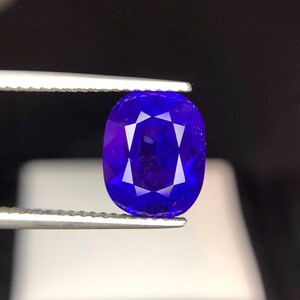 Puede incluir: Una gema ovalada de color azul intenso es sostenida por unas pinzas. La gema presenta un complejo patr&oacute;n de facetas internas, creando un efecto de estallido estelar. El fondo es oscuro, resaltando el brillo de la gema.