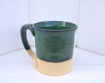 May include: A green and cream ceramic mug with a rounded handle. The mug has a dark green glaze with a lighter green glaze on the bottom.