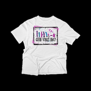 May include: White t-shirt with a graphic design of a row of colorful objects and the text "GOOD VIBES ONLY" in a black box with a pink and white splattered background.