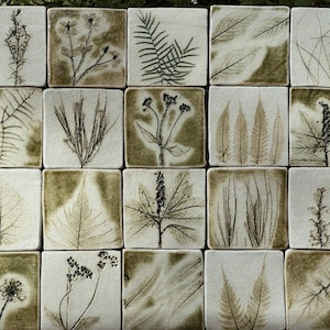 May include: A collection of twenty square ceramic tiles arranged in a grid, each featuring a unique botanical imprint. The tiles are off-white with dark green, earthy-toned plant impressions including ferns, grasses, flowers, and various leaves.