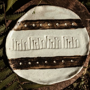 May include: A white ceramic plate with brown stripes and a textured design. The plate has a raised pattern of vertical lines and dots.