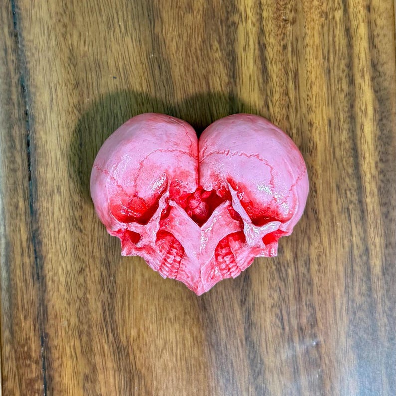 Pale pink double skull heart sculpture with red accents lying on a wooden table