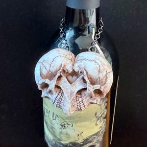 Antiqued ivory double skull heart hanging by its chains from a wine bottle against a dark background