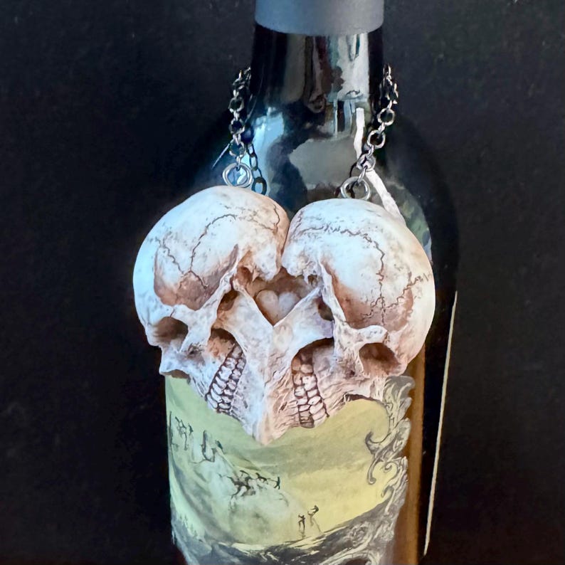 Antiqued ivory double skull heart hanging by its chains from a wine bottle against a dark background