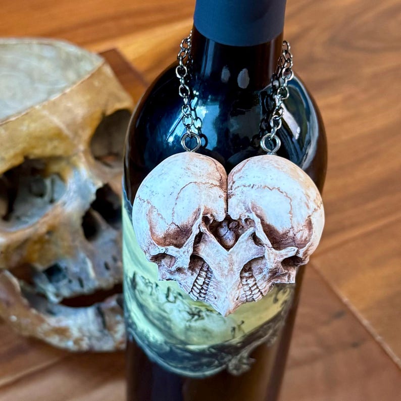 Antiqued ivory double skull heart hanging by a chain on a wine bottle, beside an aged human skull