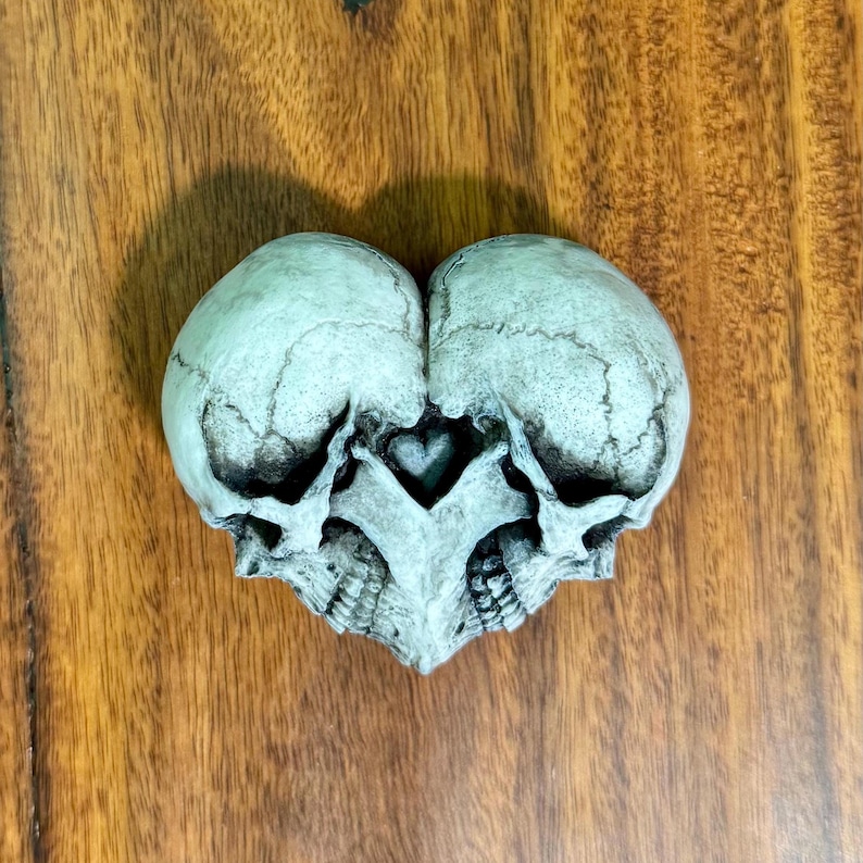 Blue-gray double skull heart sculpture on a wooden surface, front view