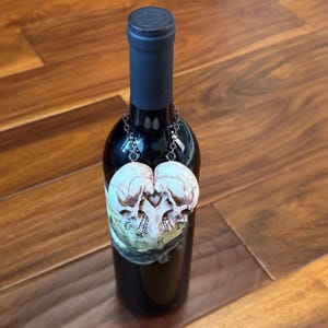 Small antiqued ivory double skull heart hanging by a chain from the neck of a wine bottle on a wooden floor