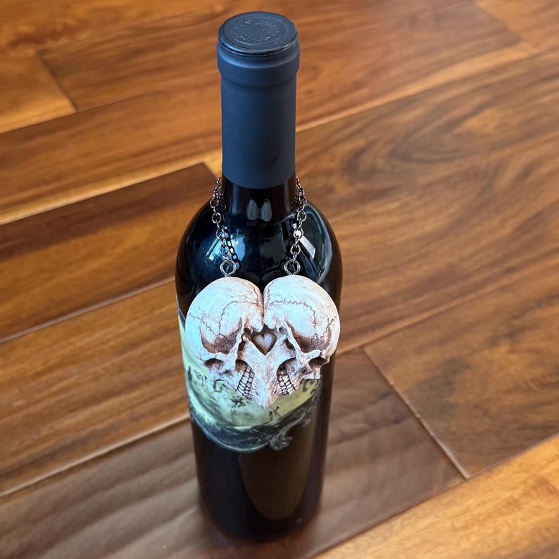 Small antiqued ivory double skull heart hanging by a chain from the neck of a wine bottle on a wooden floor